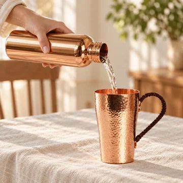 Water being poured from a copper bottle into a hammered copper mug